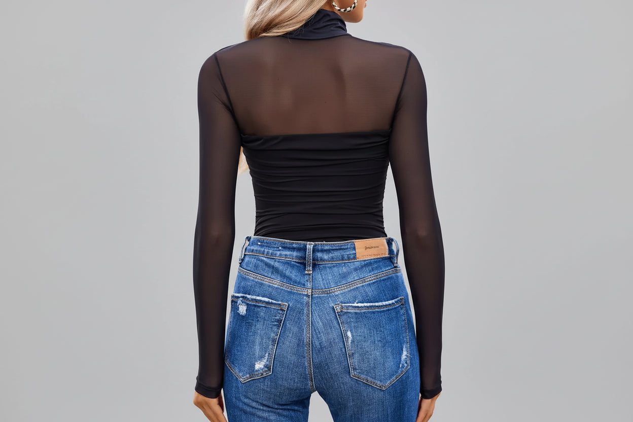 Person wearing a black sheer top and blue jeans with a blurred background