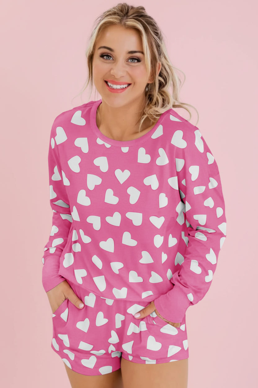 Woman wearing a pink pajama set with white heart patterns against a white background